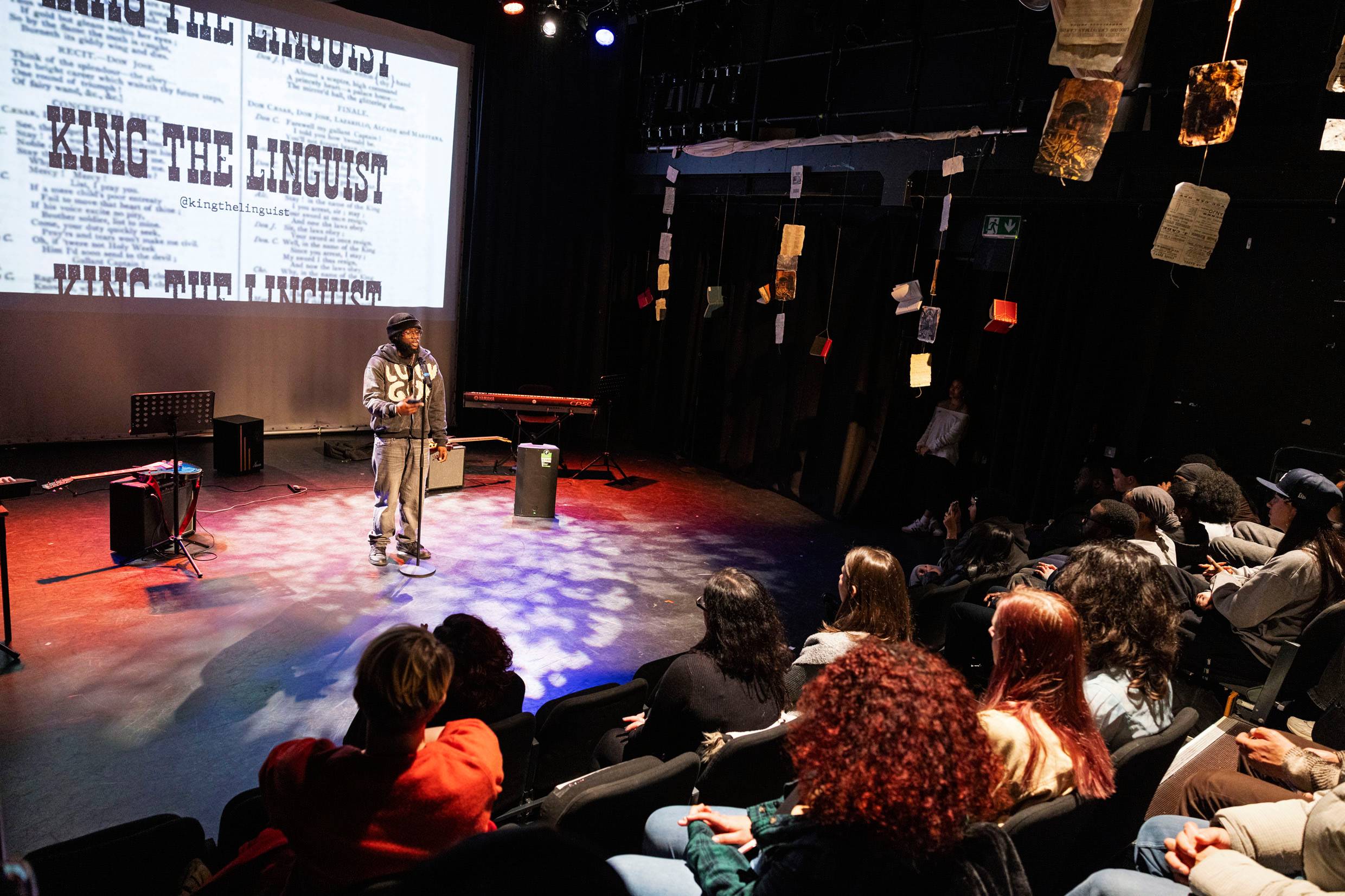 Students performs portey on a lit stage with books dangling from the ceiling