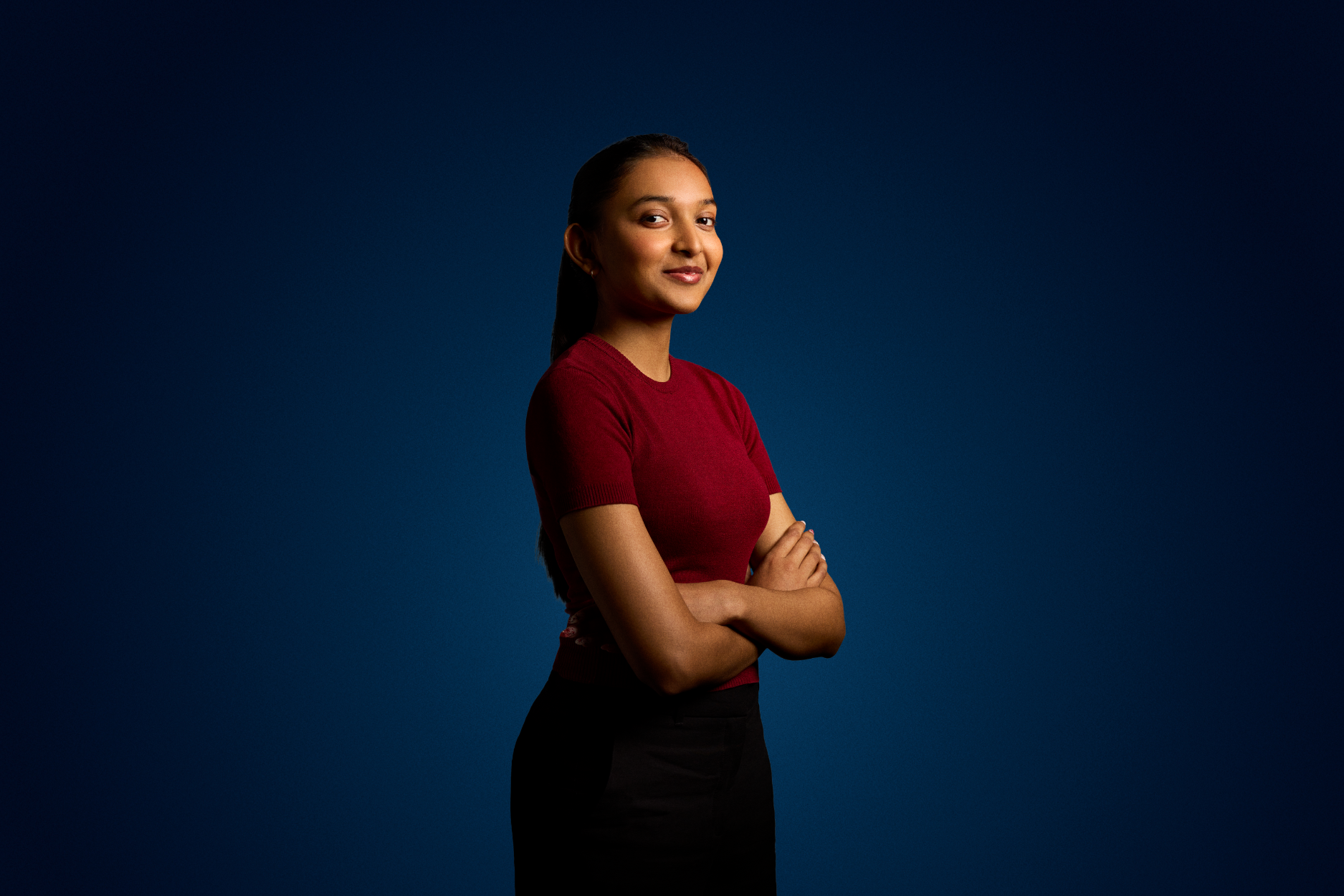 A woman stands arms folded looking at the camera on a dark blue background