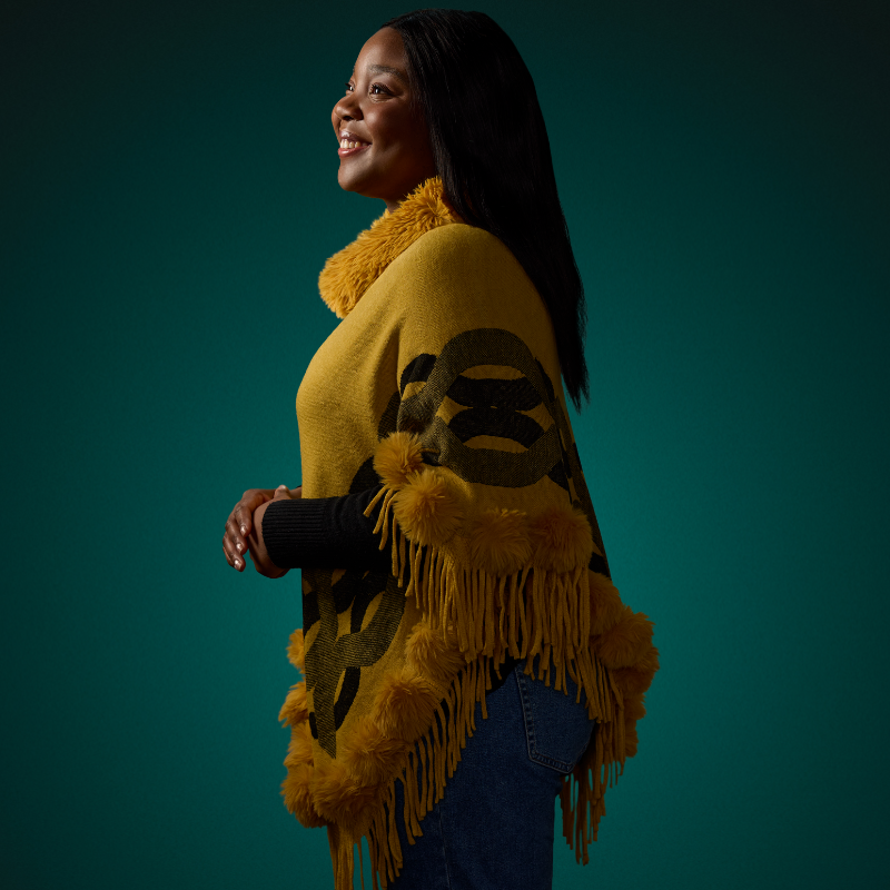 A student wearing yellow smiling and holding their hands together in front of a green background